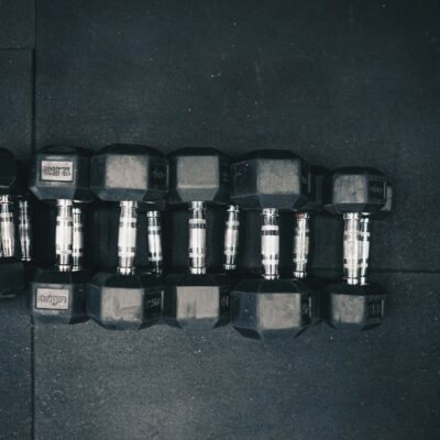 A row of black hex dumbbells with silver handles lined up in size order on a dark rubber gym floor