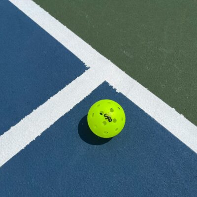 Bright yellow pickleball resting on the blue and green line of an indoor pickleball court, similar to Foxes Farm's converted barn court near Colchester