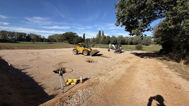 A telehandler and mini digger preparing foundations on the new stone farmyard at Bullbanks Farm, with fields and trees behind