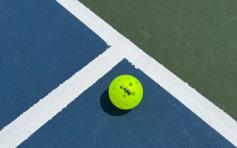 Bright yellow pickleball resting on the blue and green line of an indoor pickleball court, similar to Foxes Farm's converted barn court near Colchester
